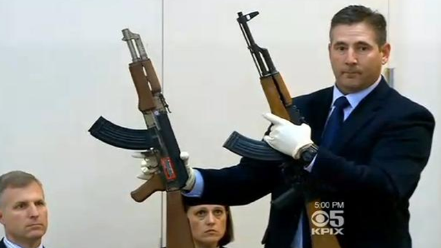 An official holds the toy gun and an AK-47 demonstrating their similarity.  