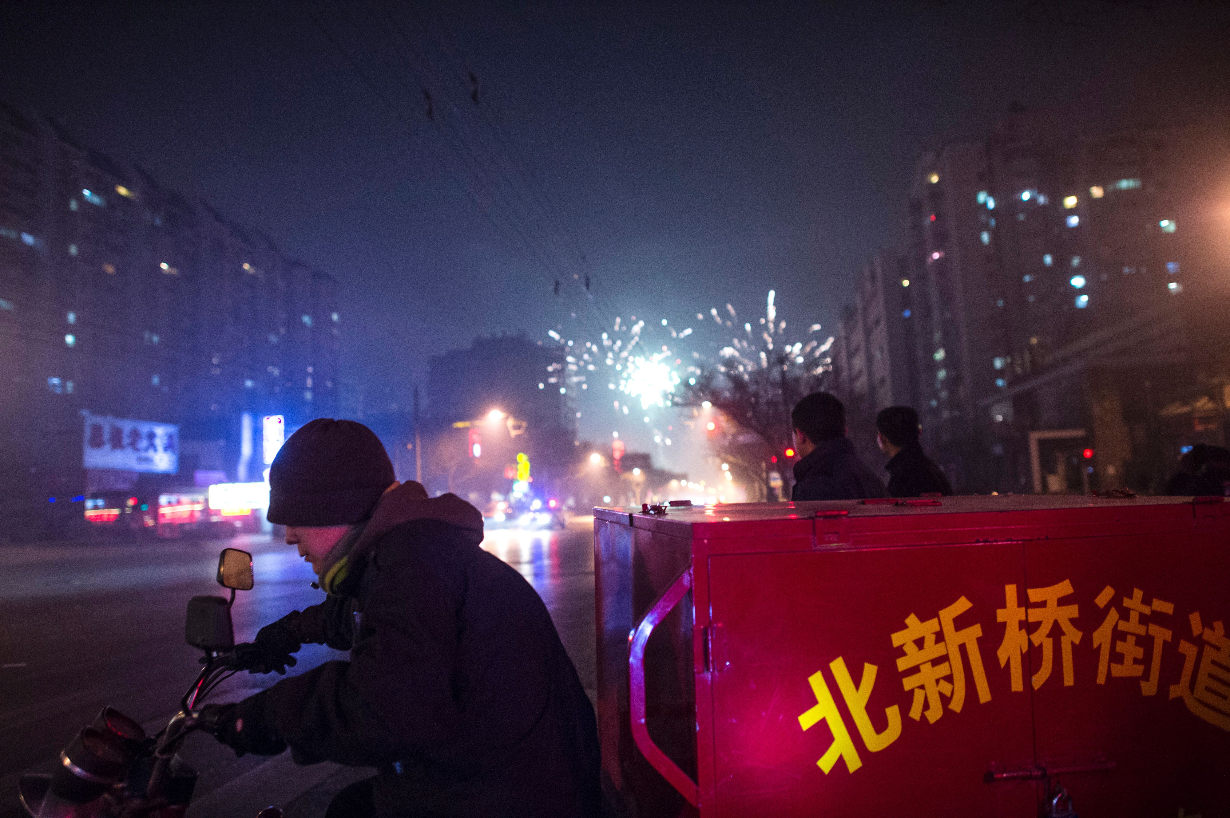 A man rides a motorcycle past people lighting fireworks on a street in Beijing on February 7, 2016, the eve of the Lunar New Year. (Getty)