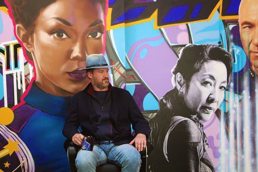 Kenneth Mitchell sitting in front of a mural of Star Trek characters