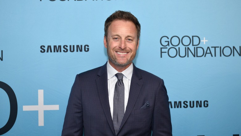 Chris Harrison standing against a blue step and repeat.