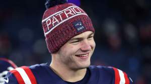 Drake Maye smiles on the Patriots sideline.