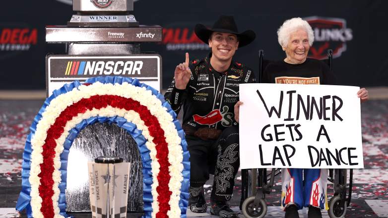 Carson Hocevar poses with trophy in victory lane after winning at Talladega alongside guest holding sign