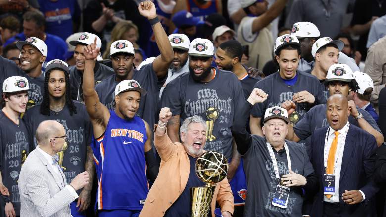James Dolan celebrates with the NBA championship trophy while Mitchell Robinson and the Knicks gather behind him after winning the 2026 NBA Finals.