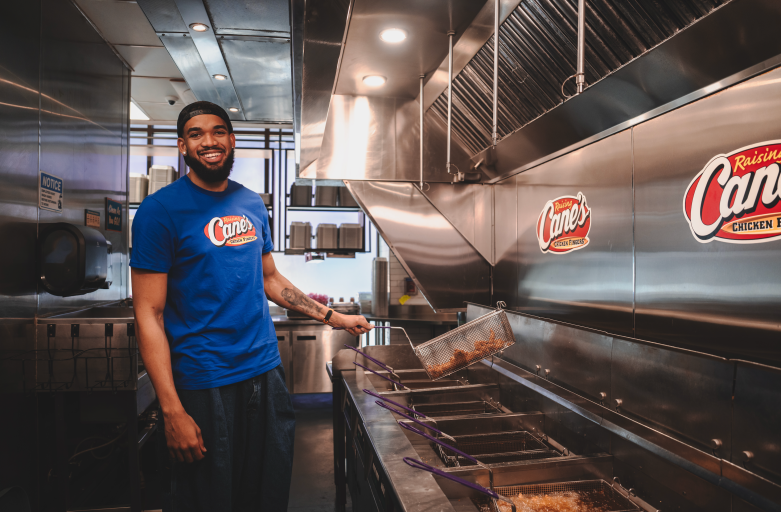 New York Knicks star Karl-Anthony Towns smiles while working at the fryer station during a celebratory shift at Raising Cane's Global Flagship in Times Square following the team's NBA championship.
