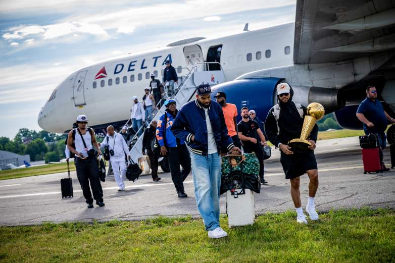 Members of the New York Knicks disembark from a Delta Air Lines charter plane in New York after winning the 2026 NBA championship, with one player carrying the Larry O’Brien Trophy following the team’s return from San Antonio.