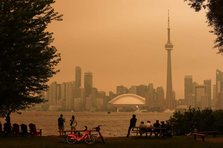 TOPSHOT - People look toward the downtown skyline from the Toronto Islands as forest fires in Northern Ontario cause poor air quality over the city, in Toronto, Ontario, Canada, July 15, 2026. Toronto had the worst air quality of any major city in the world on Wednesday, the Swiss firm IQAir said, as Canadian authorities urged people to stay indoors. Toronto edged out New Delhi and the Democratic Republic of Congo's capital Kinshasa as wildfire smoke turned the skies a hazy yellowish-grey in Canada's largest city. (Photo by Cole BURSTON / AFP via Getty Images)