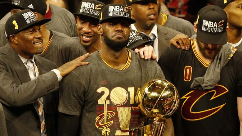 An emotional LeBron James stands beside the NBA championship trophy surrounded by Cavaliers teammates.