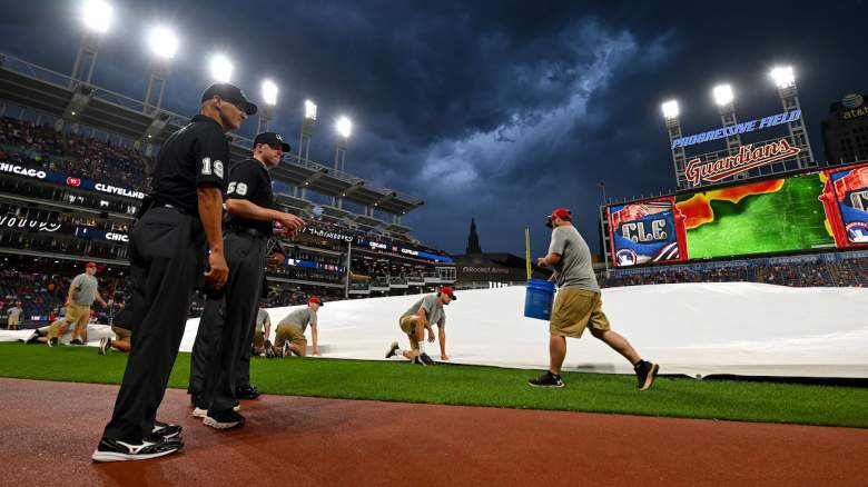 Umpire Vic Carapazza #19 and umpire Nic Lentz #59 watch as members of the Cleveland Guardians grounds crew secure the tarp